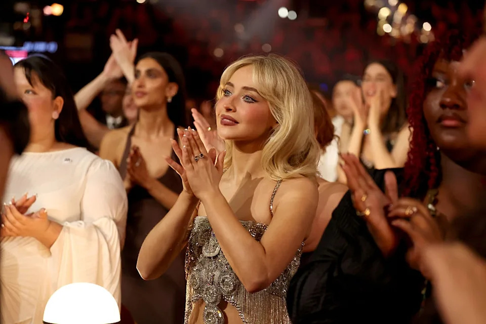 Person in an elegant outfit applauds among a standing crowd at a formal event