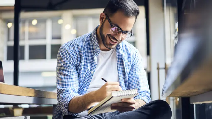A young man happily writing down money goals, budget and other financial plans inside a business.