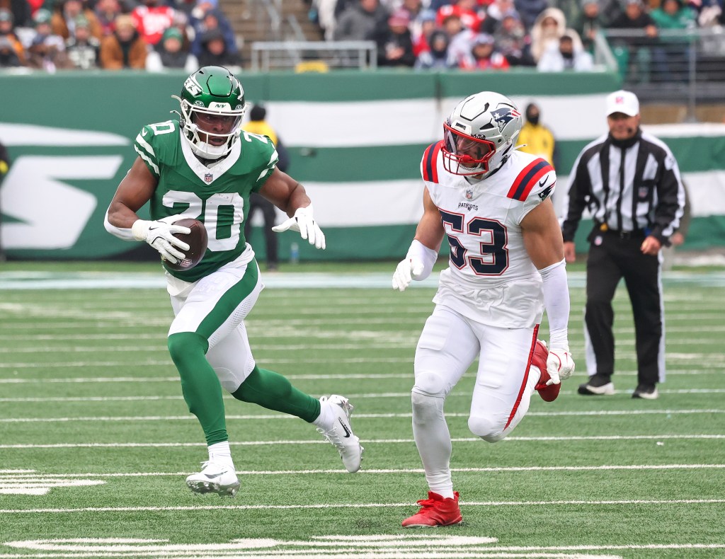 New York Jets running back Breece Hall (20) with the ball being pursued by a New England Patriots player.