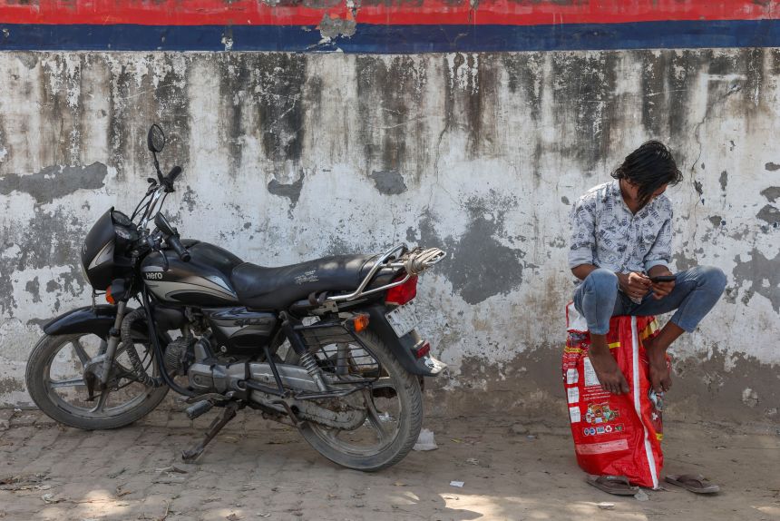 A man sits on an empty LPG cylinder as he waits outside a gas agency amid supply disruptions following the U.S.-Israeli conflict with Iran, in Noida, India, on March 11, 2026.