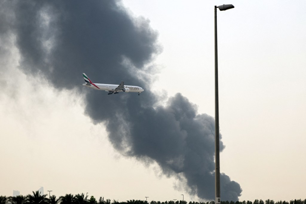 Emirates Airbus A350 aircraft landing in Dubai as a smoke plume rises from a fire.