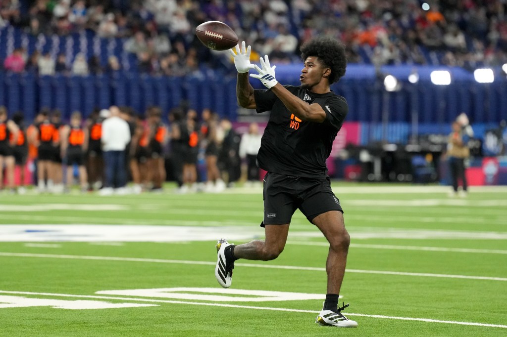 A male football player in a black shirt and shorts catches a football.