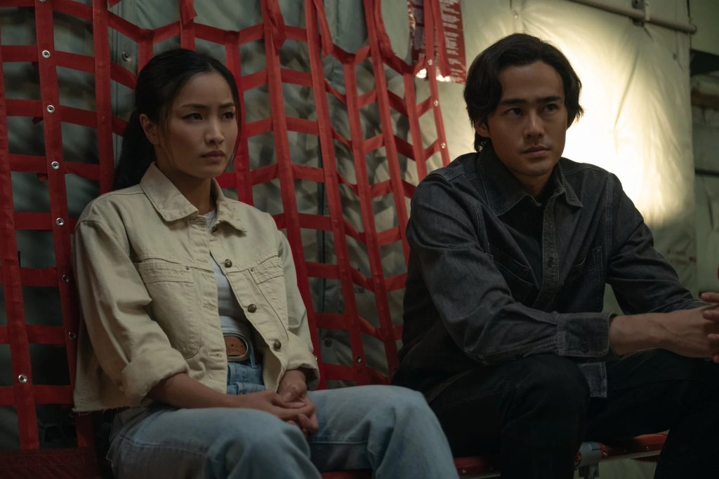 Anna Sawai and Ren Watabe sitting against red tactical webbing in Monarch: Legacy of Monsters