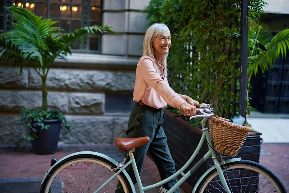 A fit middle aged woman walking while pushing her bicycle.