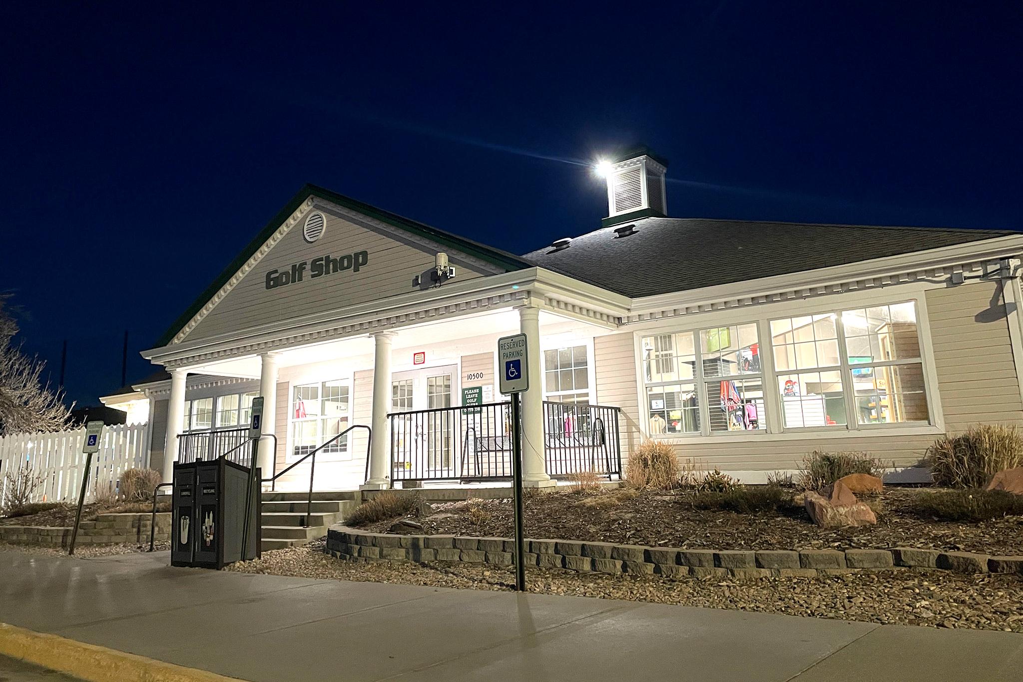 A building of white vinyl glows under a fading evening sky. Lettering spells out "Golf Shop" on the front.