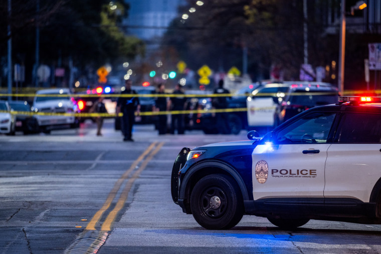 A police car parked on the street outside at a crime scene sectioned off with police tape and officers