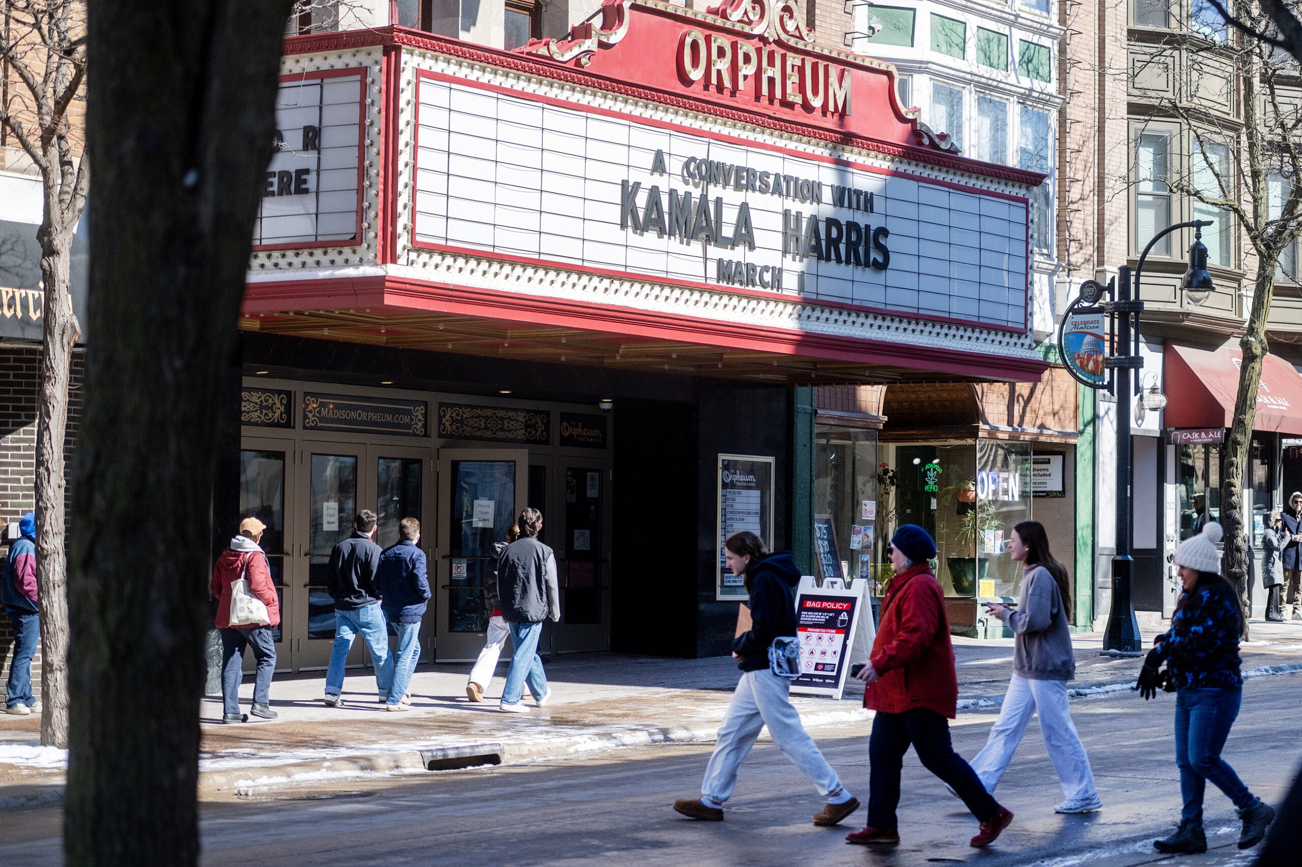 People walk past the Orpheum Theater, which has a marquee advertising “A Conversation With Kamala Harris” in March. Some snow is visible on the ground and sidewalk.