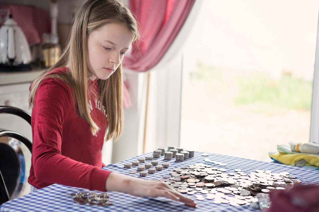Girl counting pocket money coins on a table.