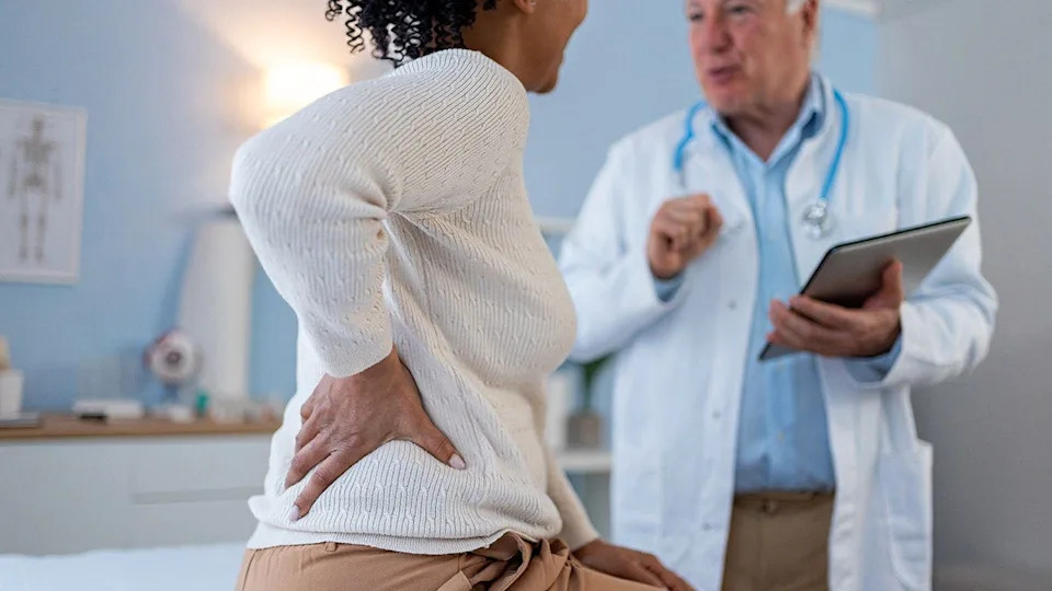 An older Caucasian male doctor examining a middle-aged African-American female patient in a doctor's office.