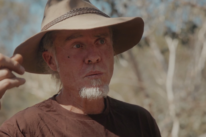 Hamish holds a finger up making a point while talking, dry bushland on his property behind him.
