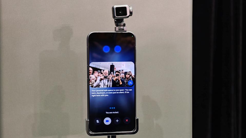 Honor's Robot Phone, a smartphone with a gimbal-mounted camera that folds out to sit on top of it, is shown on a stand at MWC displaying a live image of the reporters photographing it