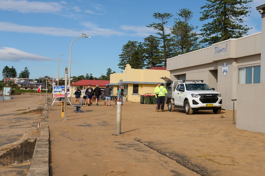 A footpath covered in sand from when waves reached the Thirroul Life Saving Club. A council vehicle is seen next to the building