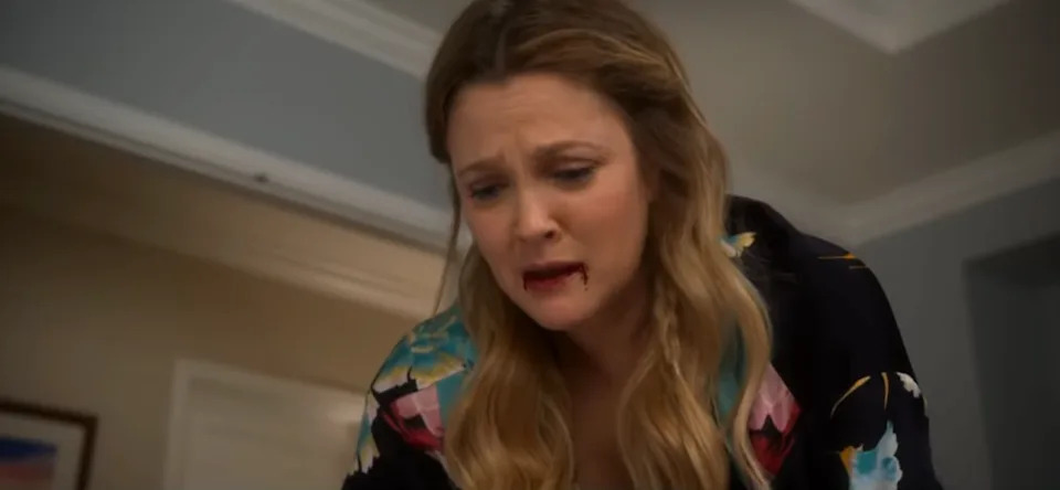 A person with long hair, in a floral-patterned outfit, looks distressed with blood at corners of their mouth, gazing downward