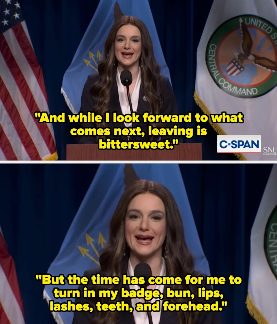 Person speaking at a podium with flags and a C-SPAN logo, dressed formally in a dark suit with long wavy hair