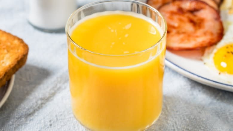 Glass of orange juice on a table with fried ham, sunny side-up eggs, and toast
