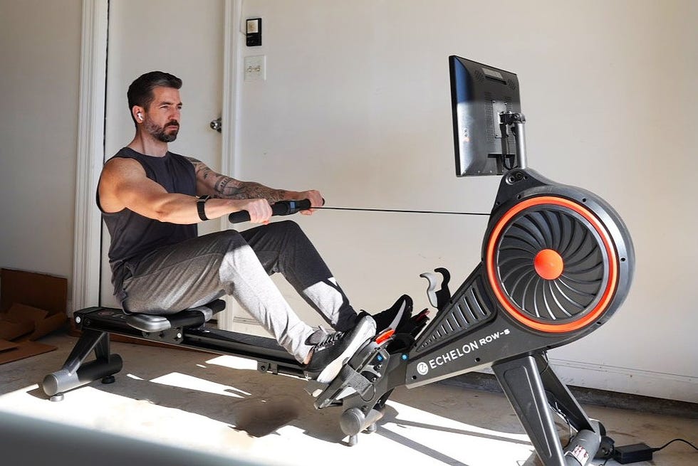 person using a rowing machine with a monitor in a home setting