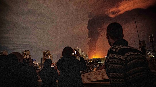 Residents of Tehran look on as flames and smoke rise from an oil storage facility struck by Israeli troops.