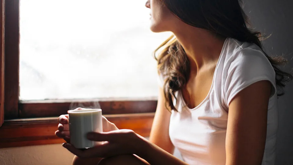 Woman wearing a white t-shirt drinking a hot drink by the window