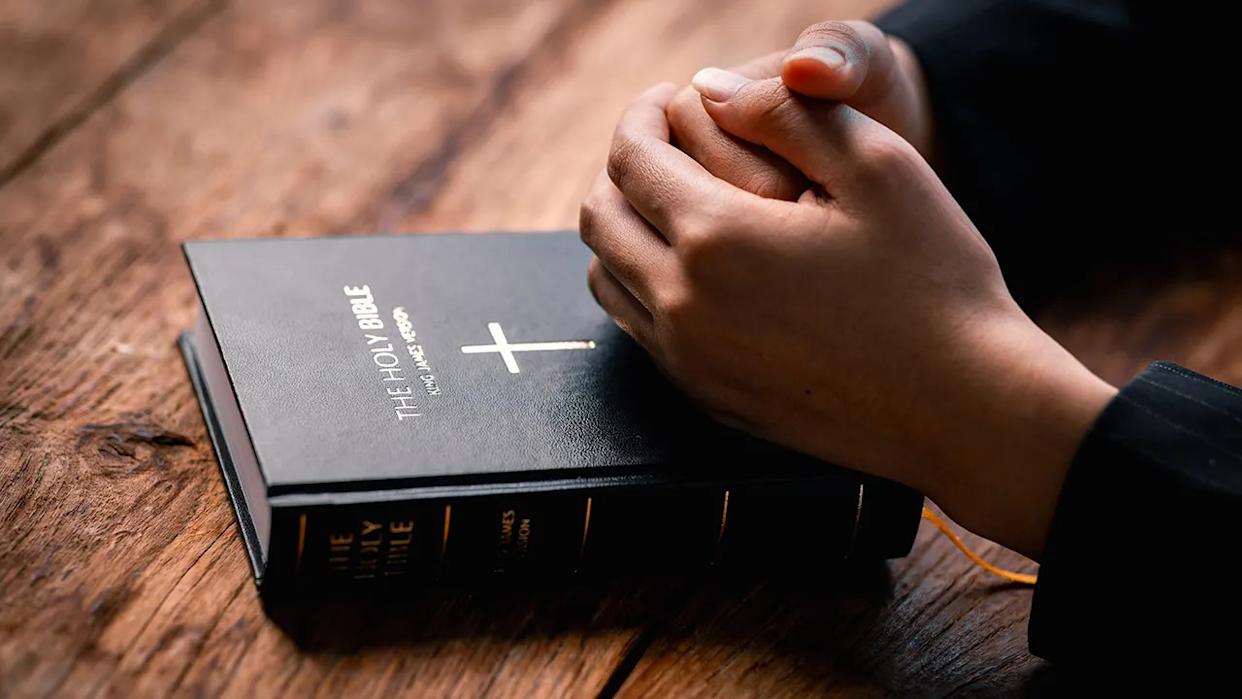 Hands folded in prayer on a Holy Bible in church