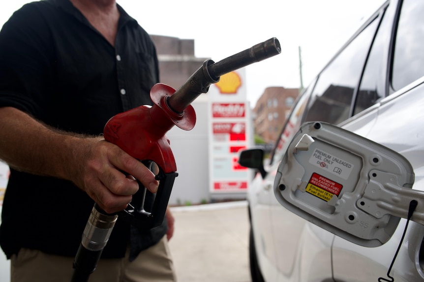 A man holds a petrol nozzle next to his car.
