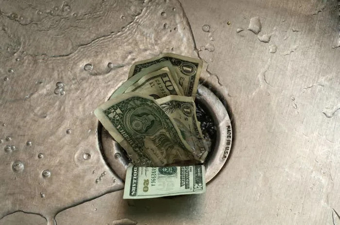 Dollar bills partially wet in a sink drain with scattered water droplets around