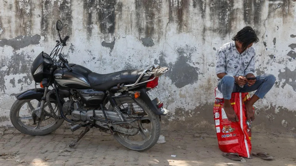 A man sits on an empty LPG cylinder as he waits outside a gas agency amid supply disruptions following the U.S.-Israeli conflict with Iran, in Noida, India, on March 11, 2026. - Bhawika Chhabra/Reuters