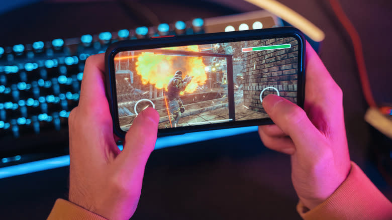 two holds holding a smartphone while playing a game with touch screen controls next to a mechanical keyboard