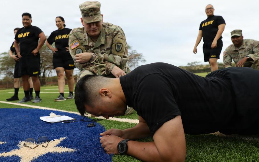 A soldier does a plank while a uniformed soldier bends down and looks at him.