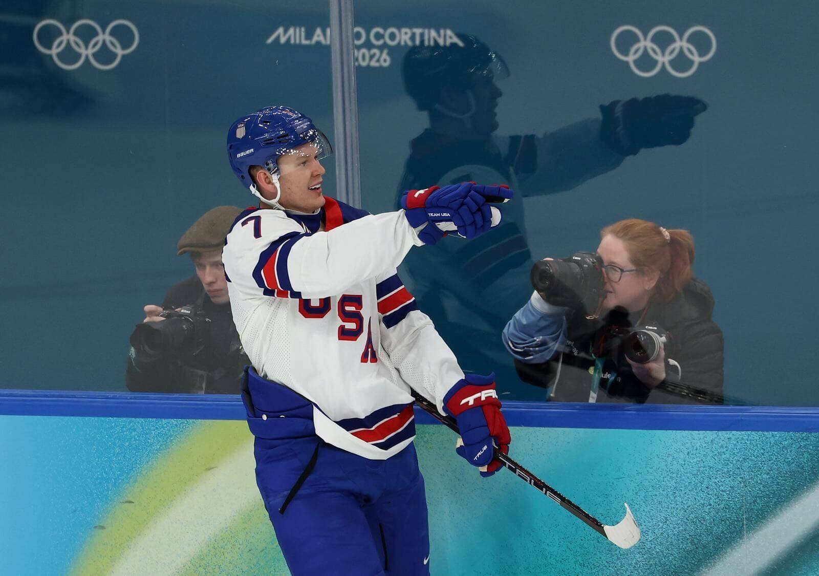 Brady Tkachuk gestures during a Team USA game with two photographers visible behind the glass.