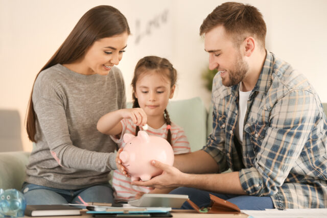 Little girl with her parents sitting on sofa and putting coin in