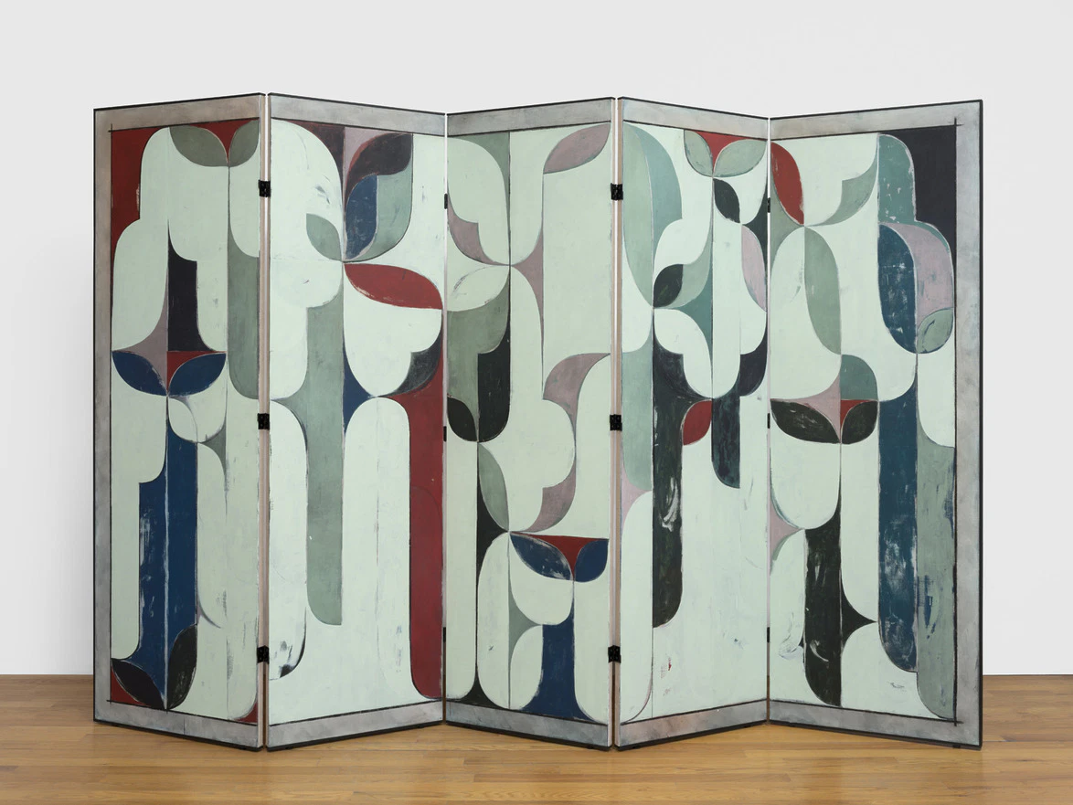 Folding room divider with abstract geometric patterns in green, red, black, and white on a wooden floor background.