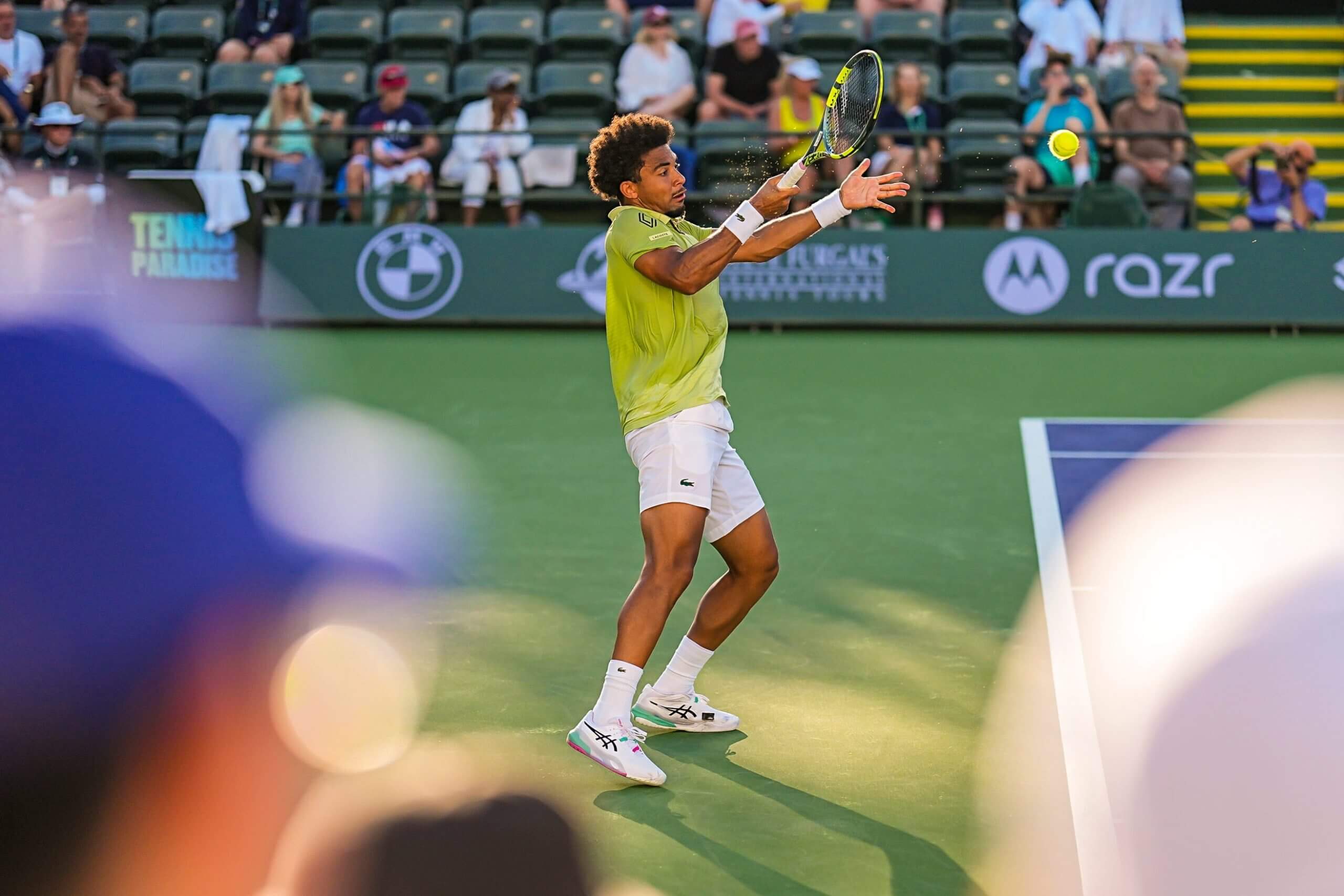 Arthur Fils hits a forehand on the green behind a purple tennis court, as seen from the stands at the side of the court.