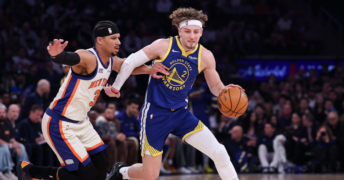 A Golden State Warriors player dribbles the basketball while being closely guarded by a New York Knicks player during a game.