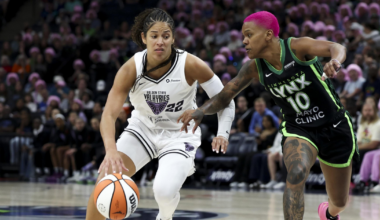 A basketball player in a white Golden State Valkyries uniform dribbles the ball while a Minnesota Lynx player with bright pink hair defends closely.