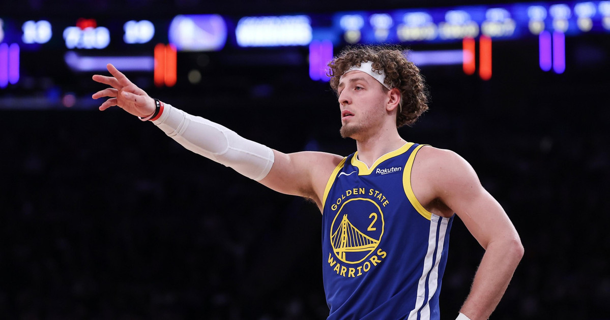 A Golden State Warriors player with curly hair points with his left arm extended, wearing a blue jersey numbered 2 and a white arm sleeve.
