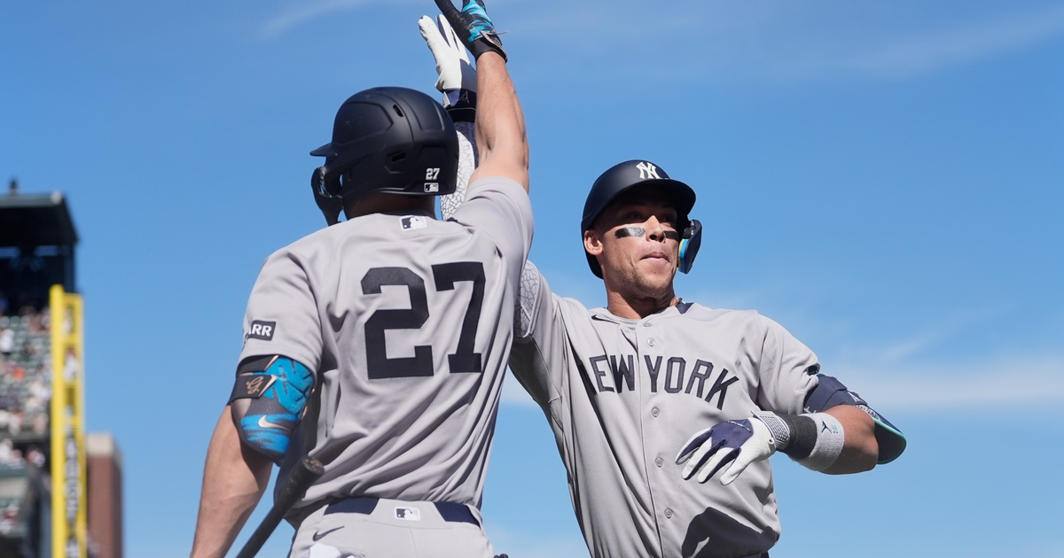 Two New York Yankees baseball players in gray uniforms high-five each other during a bright, sunny game.