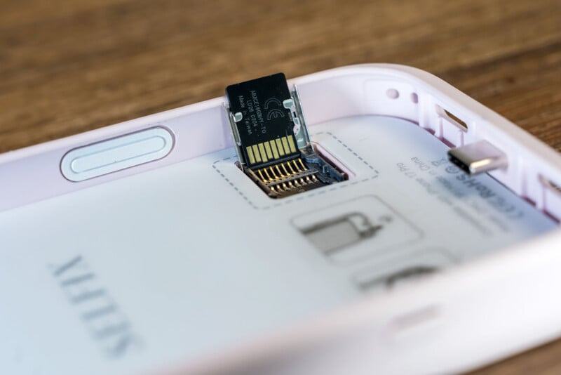A close-up of a microSD card partially inserted into a slot inside a white electronic device, with connection pins visible and instruction graphics printed on the device.