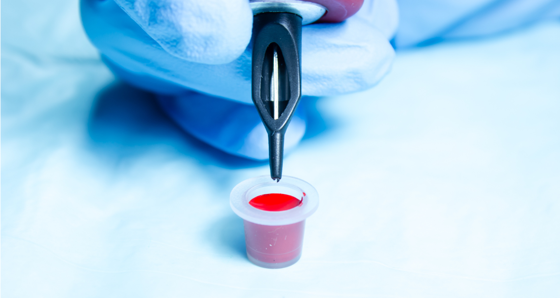 A person holding a tattoo needles with a pot of red ink.