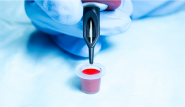 A person holding a tattoo needles with a pot of red ink.