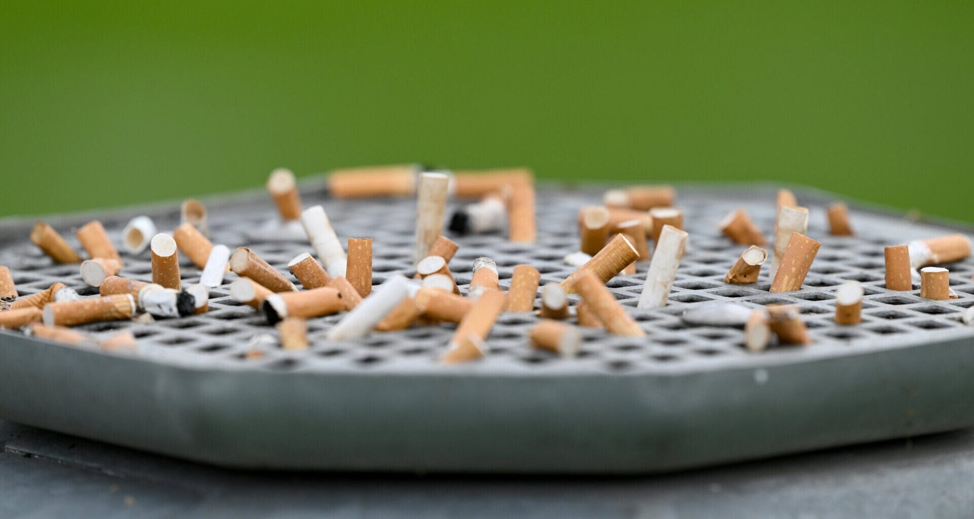 Cigarette butts stuck on a garbage can with an ashtray.