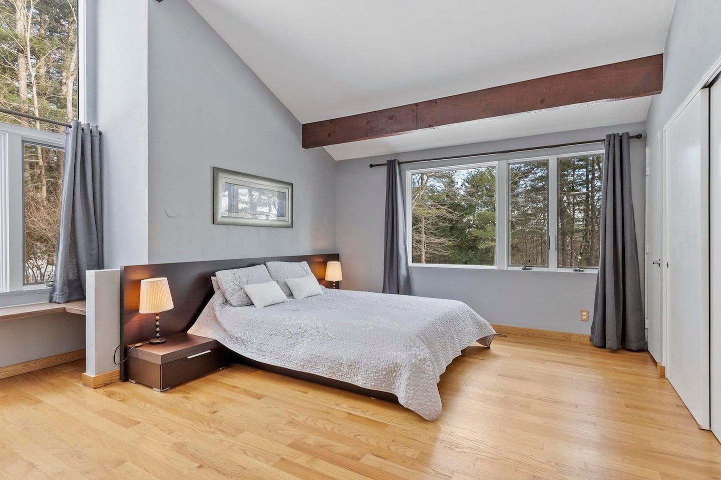 Above: The peaked ceiling and wood beams continue in the primary bedroom. Below: The accompanying bathroom has a set of unique windows.