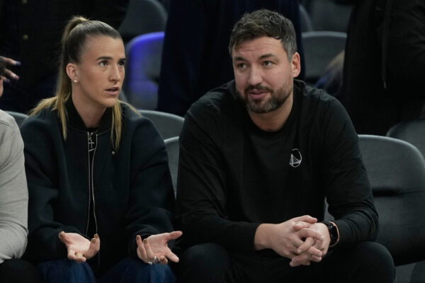 New York Liberty's Sabrina Ionescu, left, sits with Golden State Warriors assistant coach and Liberty head coach Chris DeMarco before an NBA basketball game between the Warriors and the Utah Jazz in San Francisco, Monday, Nov. 24, 2025. (AP Photo/Jeff Chiu)