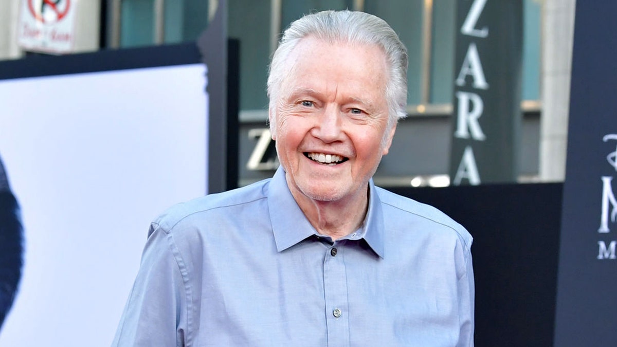 Jon Voight smiling in a blue collared shirt.