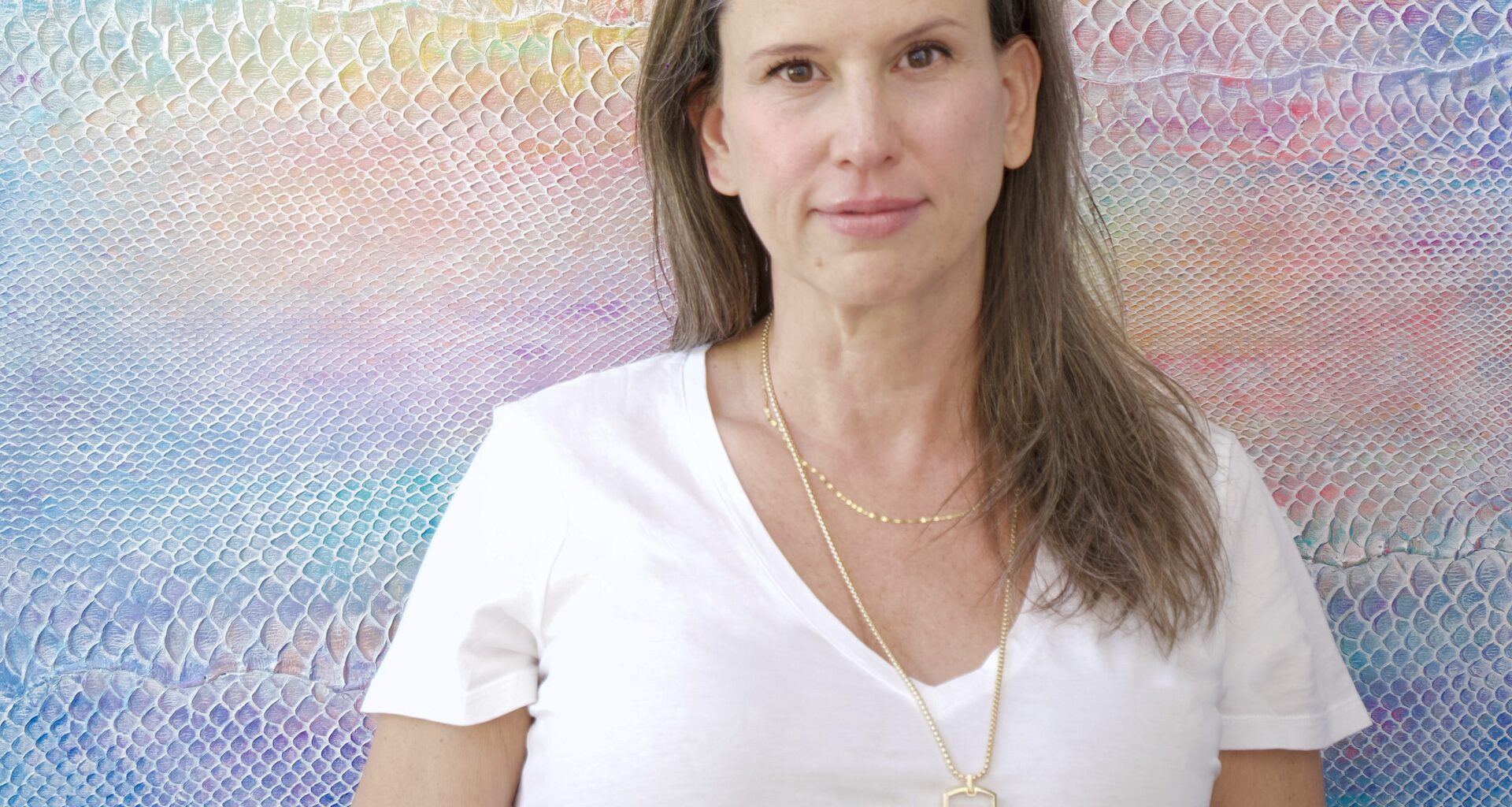 Artist Laura Shape stands in front of a colorful painting made of the skin of an invasive python species.