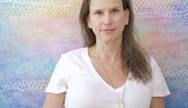 Artist Laura Shape stands in front of a colorful painting made of the skin of an invasive python species.