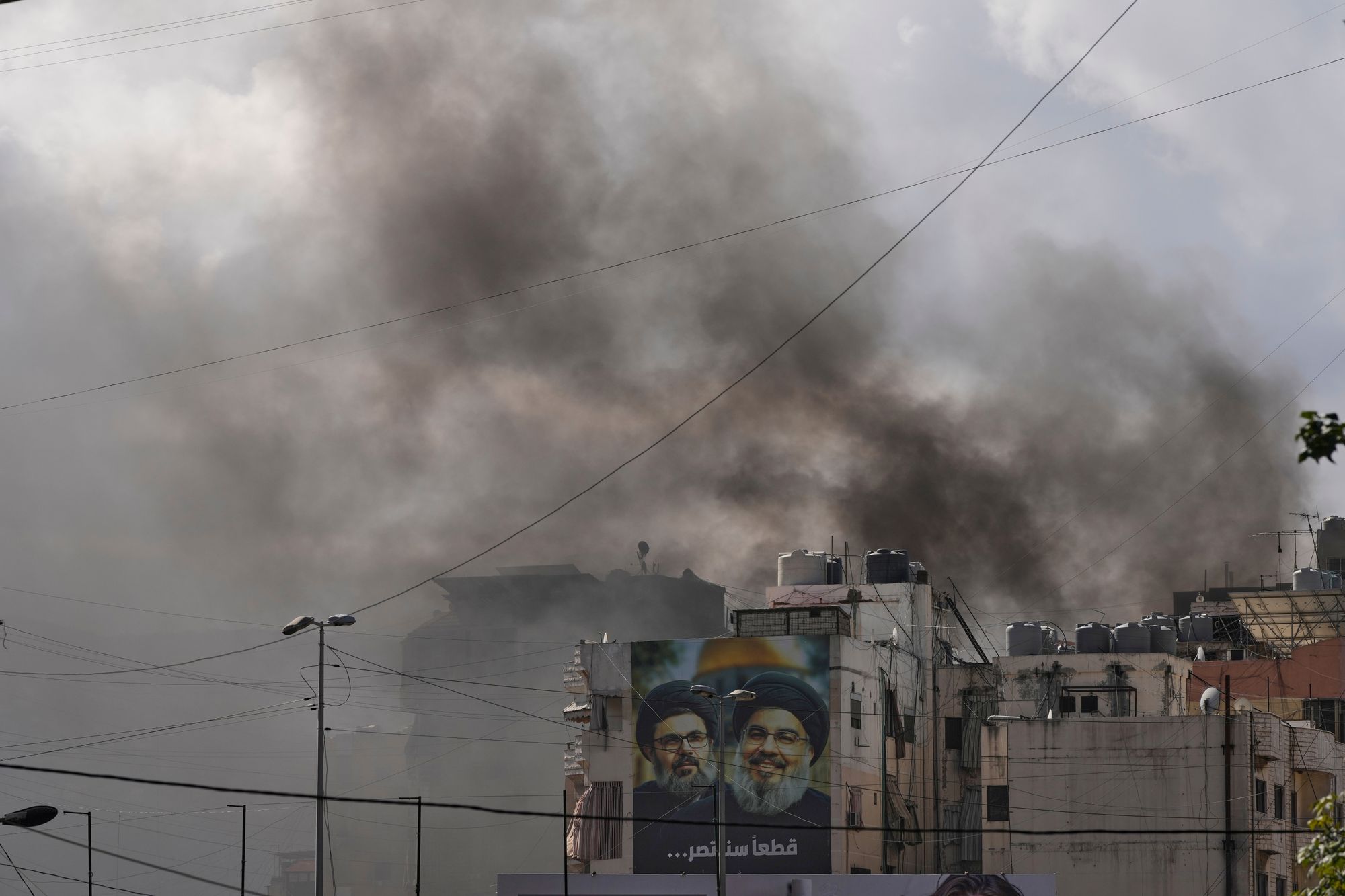Portraits of Hezbollah's late leaders Hassan Nasrallah, right, and his cousin, Hashem Safieddine, are seen, as smoke rises following an Israeli airstrike in Dahiyeh, Beirut's southern suburbs, on Monday