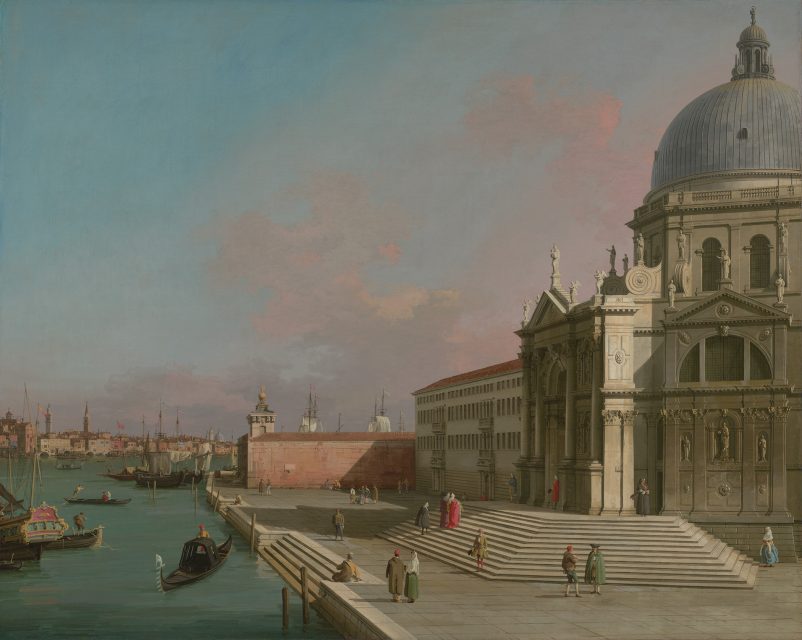 A view of a grand domed building beside a canal in Venice with people walking, gondolas in the water, and a clear blue sky.