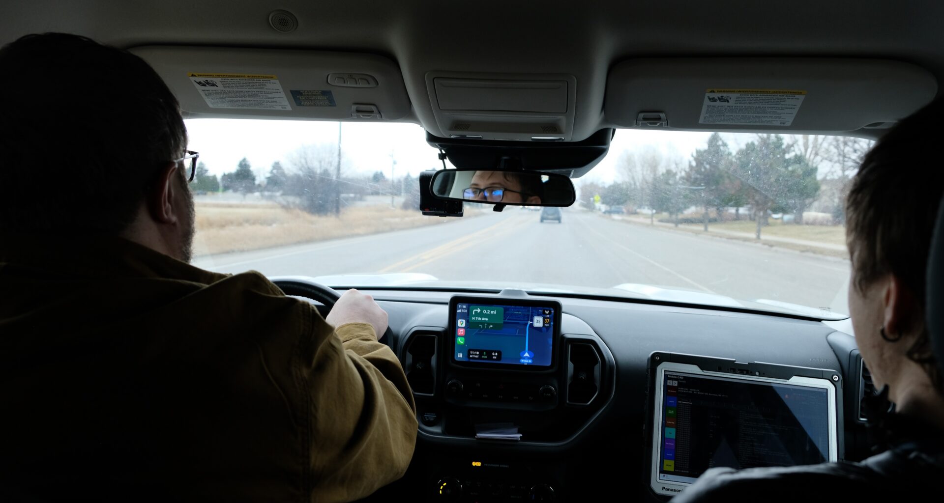 A photo from the back seat of a car, two men in the front and passenger seat driving