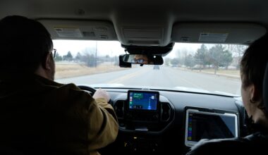 A photo from the back seat of a car, two men in the front and passenger seat driving