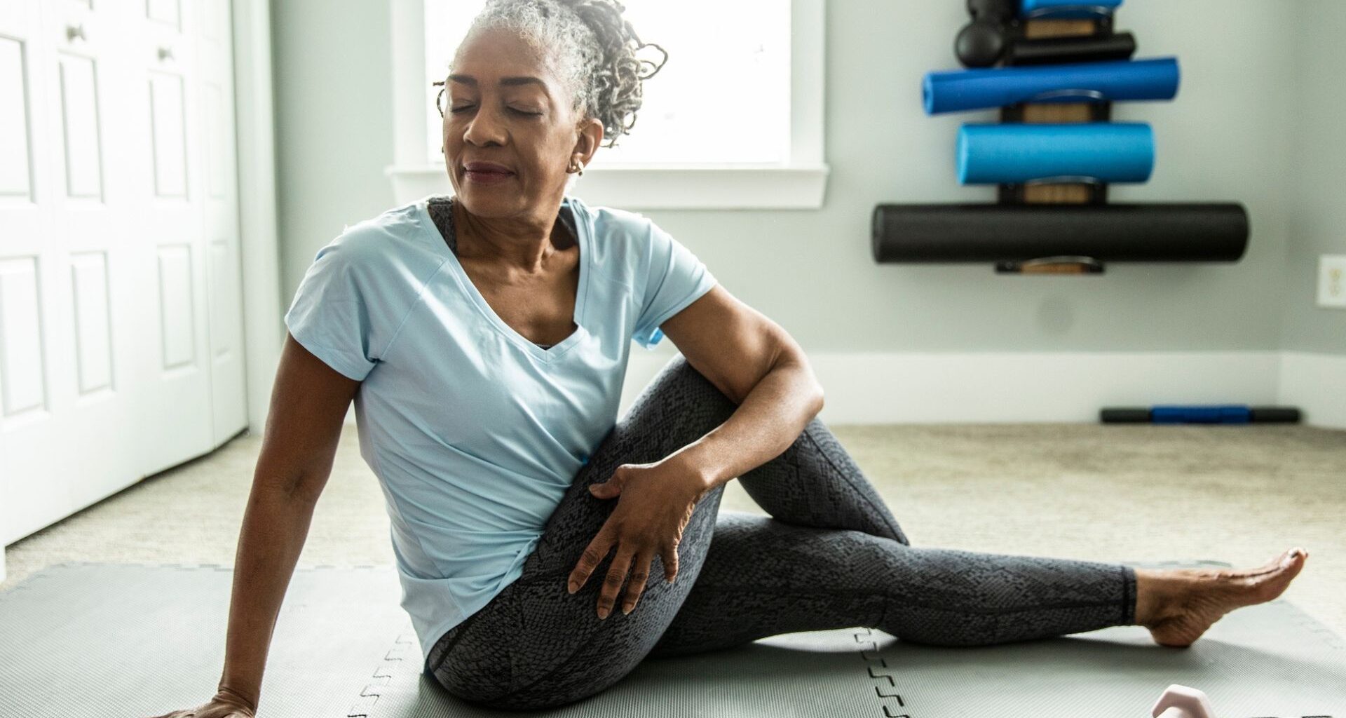 woman sitting on an exercise mat wearing leggings and tshirt in a seated twist facing the camera with her eyes closed.